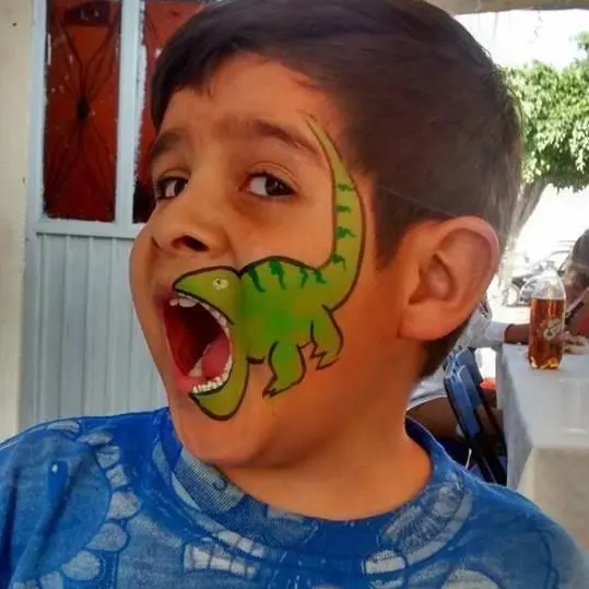 Niño con pintacaritas de dinosaurio, rugiendo en plena fiesta