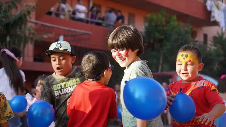 Niños con capas y pintacaritas jugando con un globo
